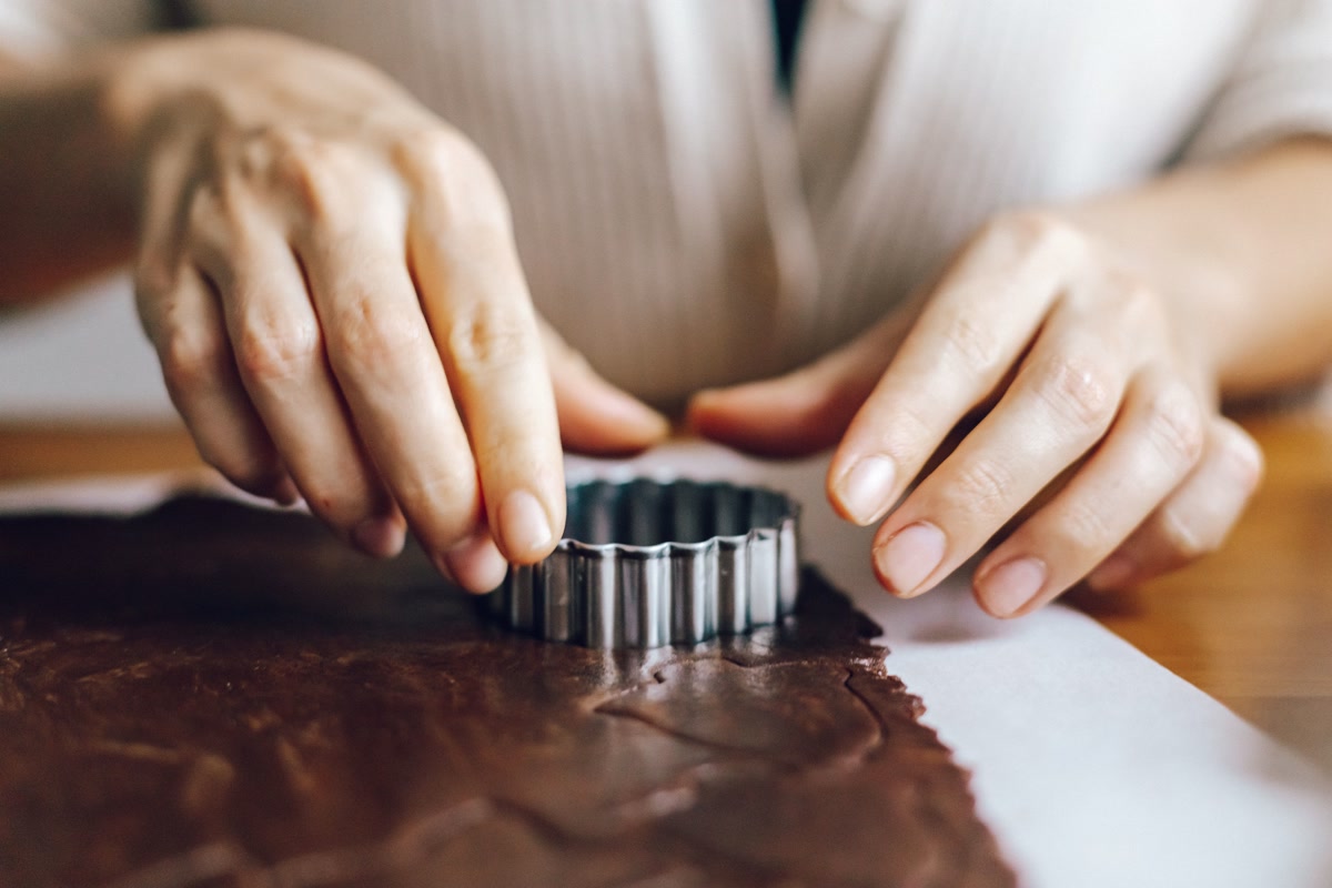 Hands pressing cookie cutter into dough to make homemade dog treat shapes