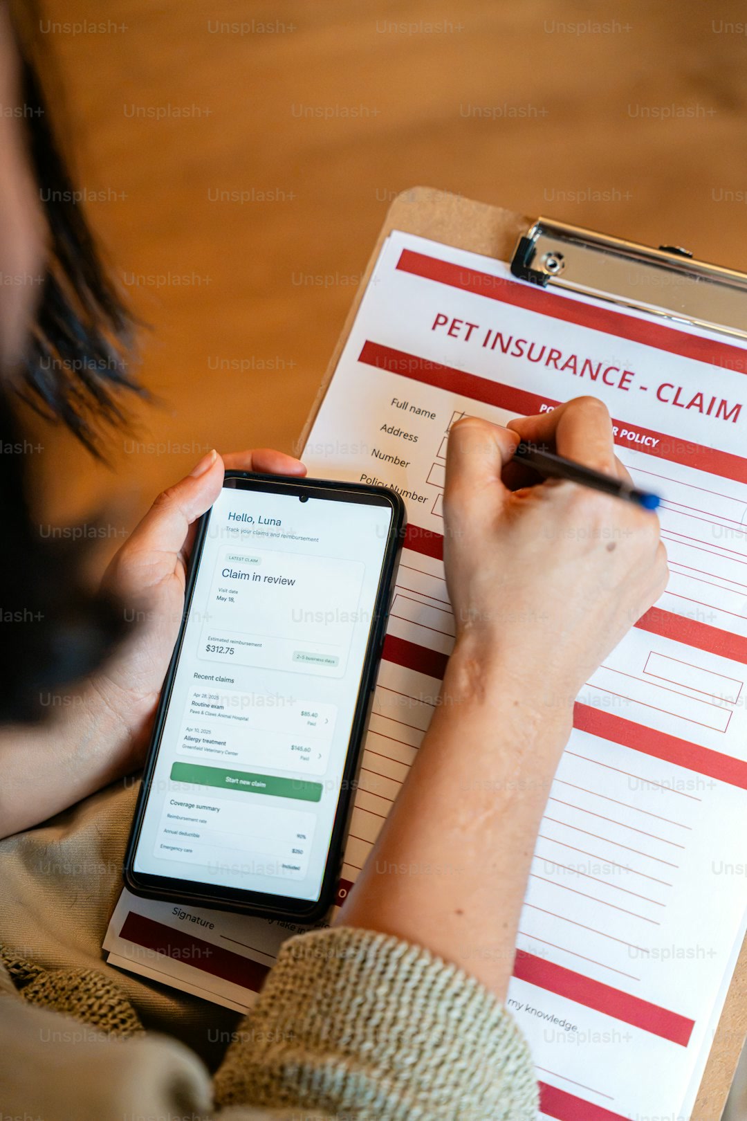 Hands filling pet insurance claim form, using smartphone