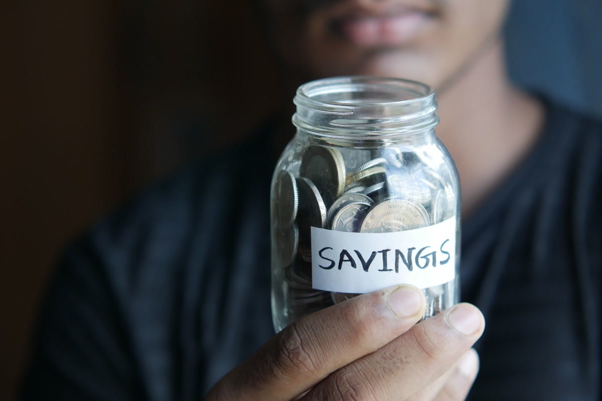 Glass jar labeled savings filled with coins for building pet emergency fund