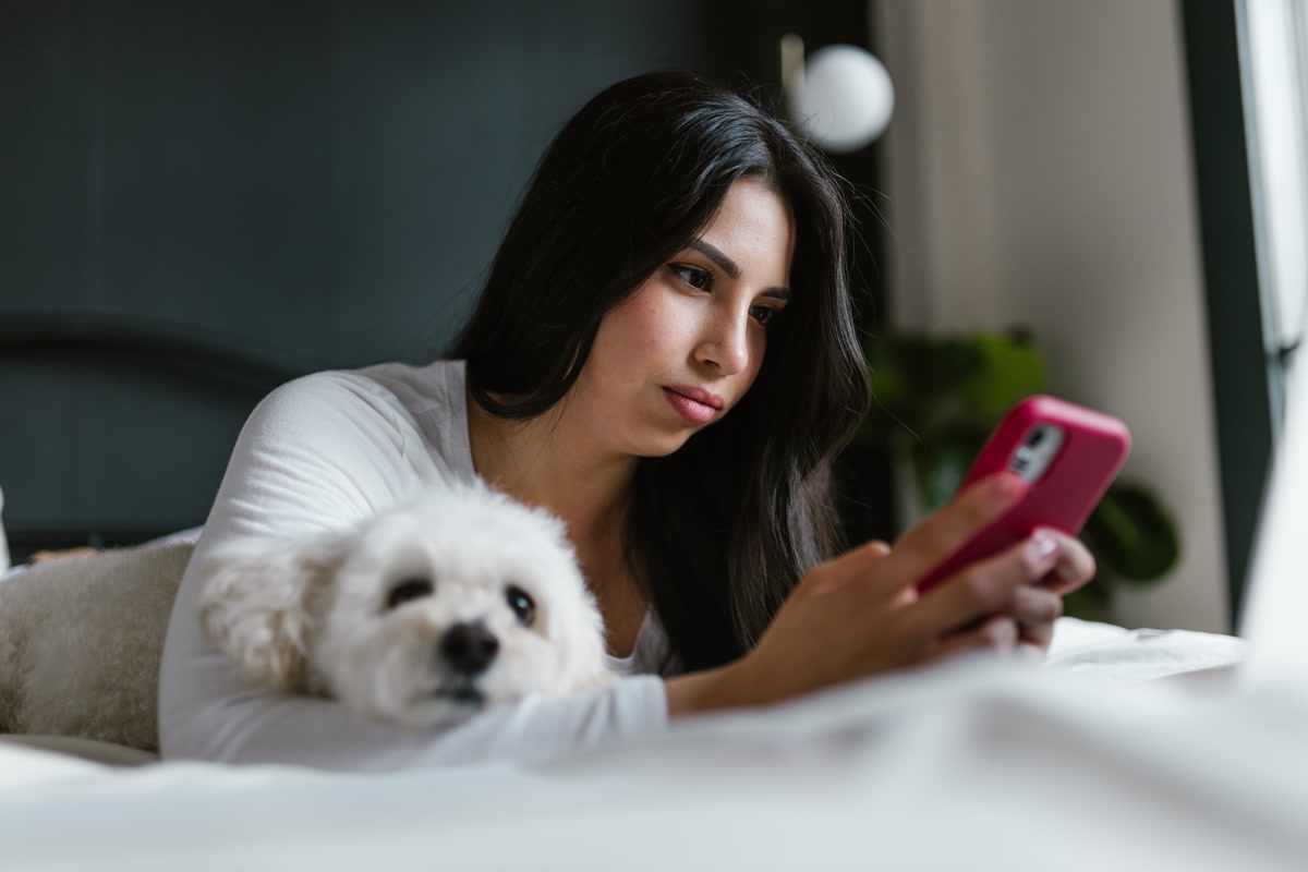 Woman using phone to monitor pet remotely while dog rests nearby